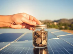 un piccolo barattolo in vetro con delle monete all'interno su dei pannelli fotovoltaici